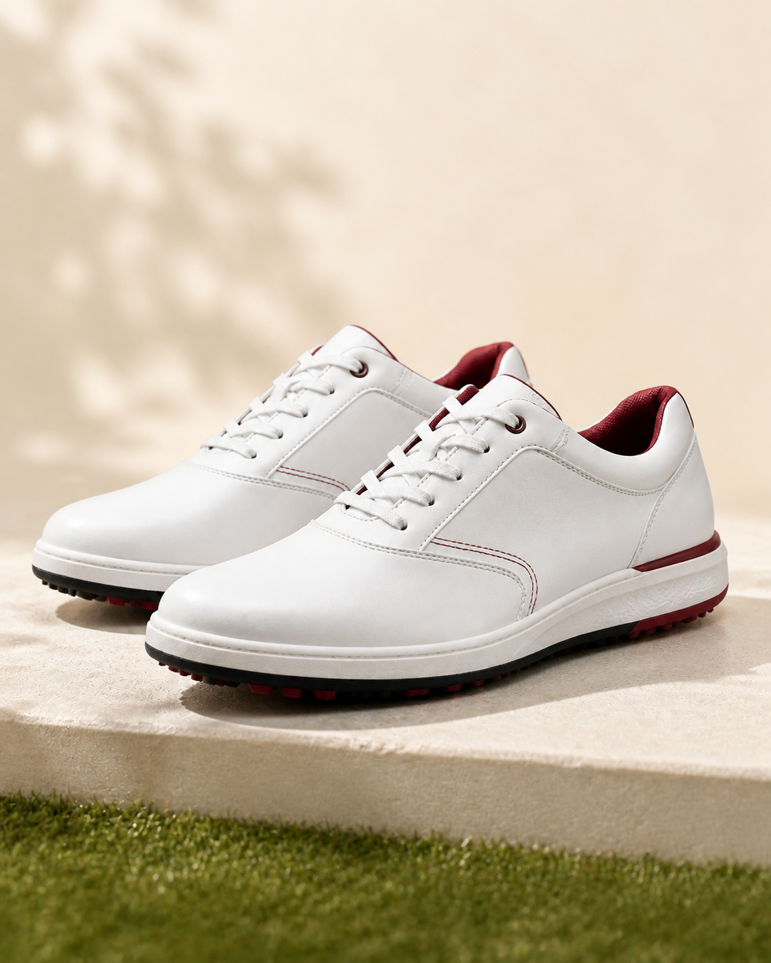 Pair of burgundy and white spikeless golf shoes on a warm studio floor
